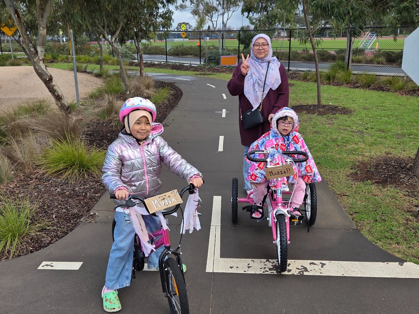 Maria on her pink tricycle on a bike path, with Muna riding beside her and Mum behind them
